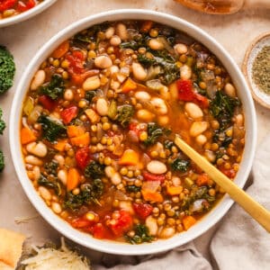 lentil and white bean soup in a white bowl with gold spoon inserted.