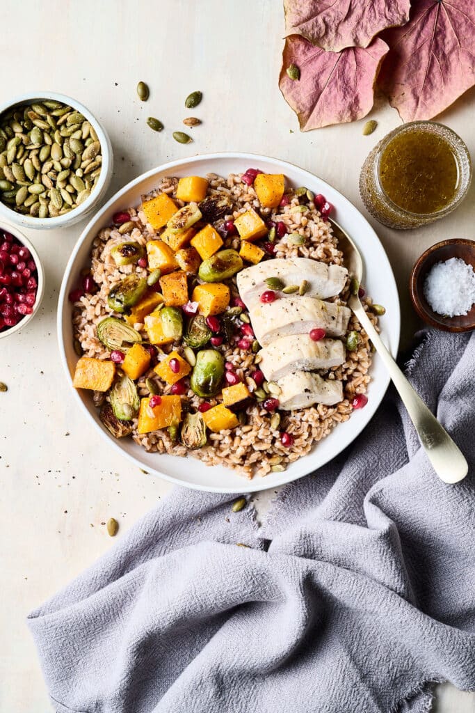 harvest grain bowl with chicken in a bowl with ingredients surrounding it.