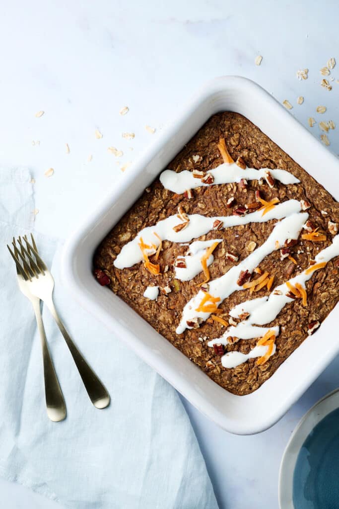 carrot cake baked oats recipe in a baking dish with protein frosting and shredded carrots on top.