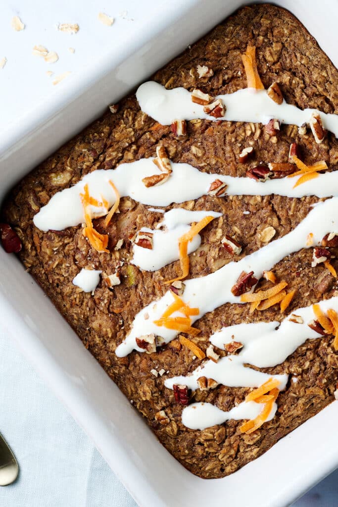 carrot cake baked oats in a baking dish with cream cheese frosting on top.