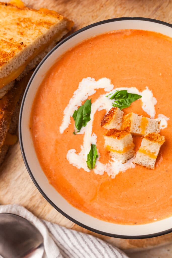 high protein tomato soup topped with basil leaves, croutons and cream in a bowl.