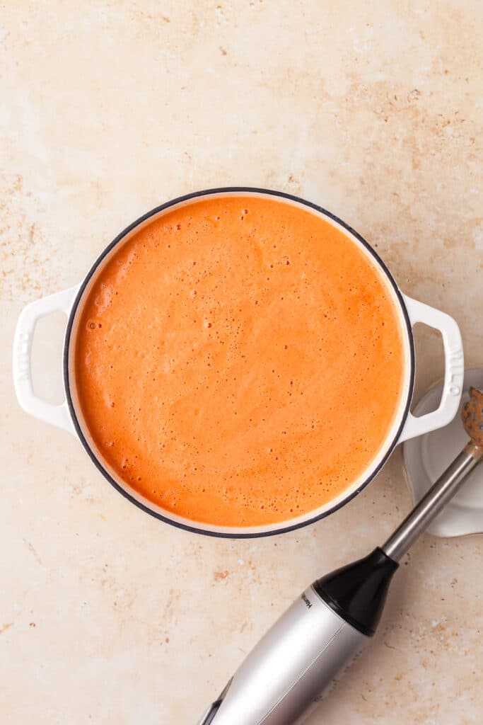 high protein tomato soup in a stock pot with immersion blender next to it.