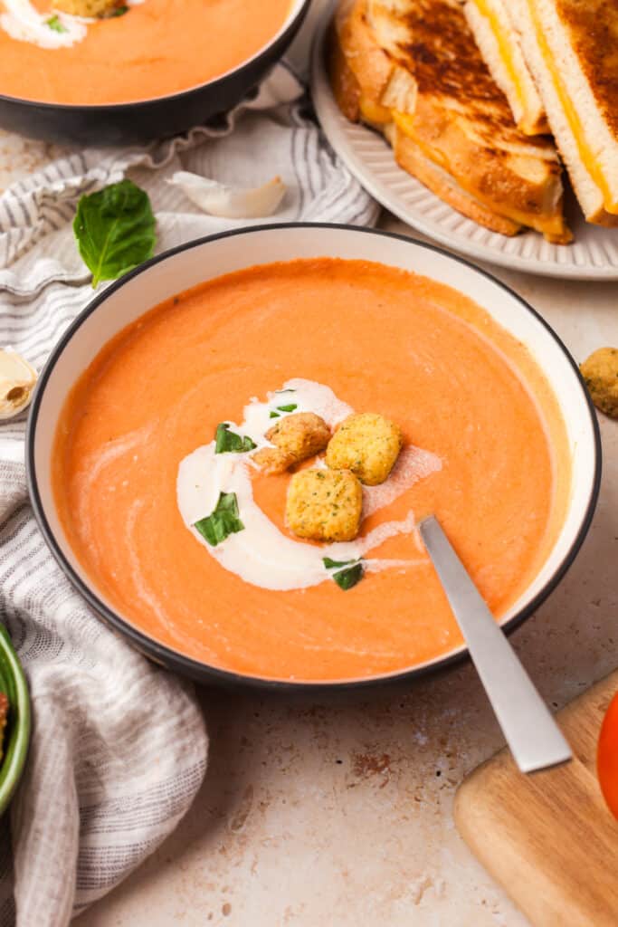 high protein tomato soup topped with basil leaves, croutons and cream in a bowl.
