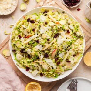 shaved brussels sprout salad on a white plate with ingredients surrounding it.