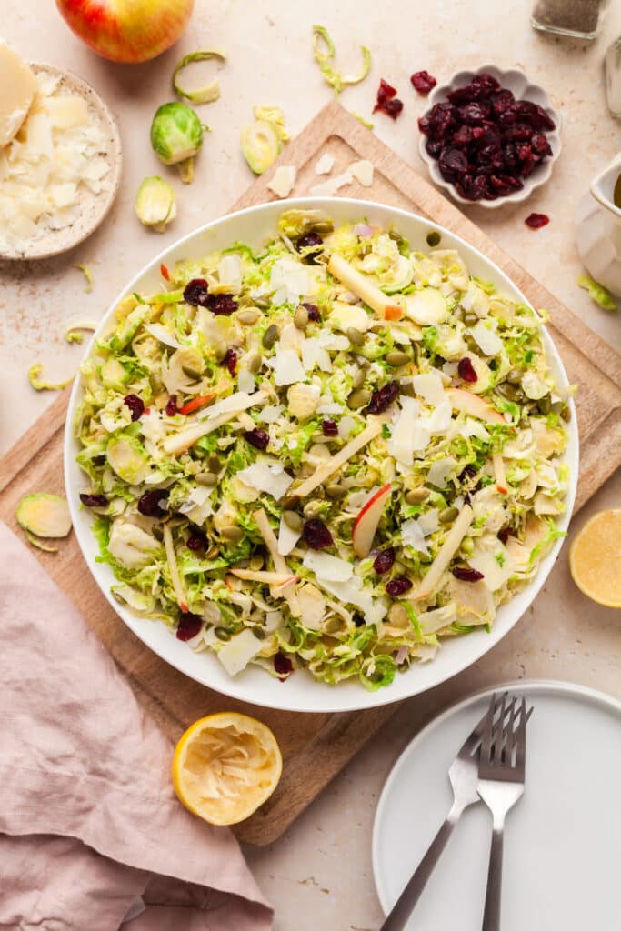 shaved brussels sprout salad on a white plate with ingredients surrounding it.