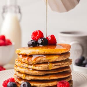 stack of pcos friendly pancakes with berries and syrup being poured over.