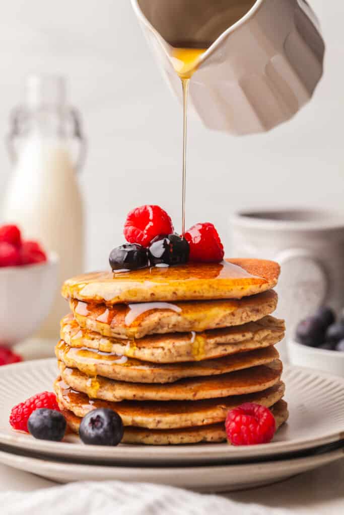 stack of pcos friendly pancakes with berries and syrup being poured over.