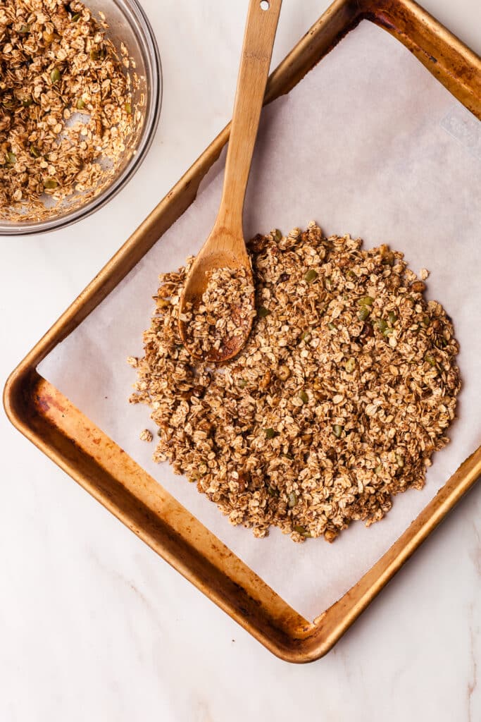 granola mixture being spread onto parchment lined baking sheet.