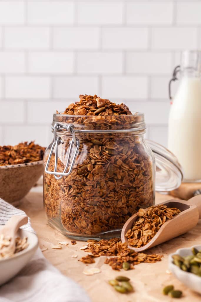 pcos friendly granola in glass jar with wooden scoop next to it.