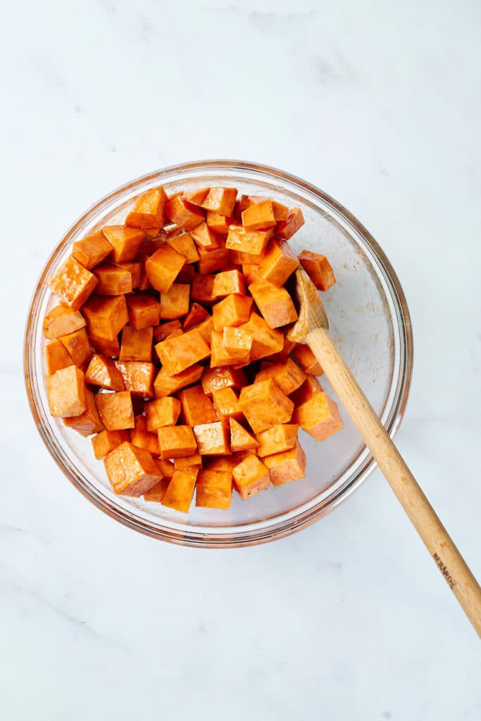 sweet potato cubes in a glass bowl with wooden spoon.