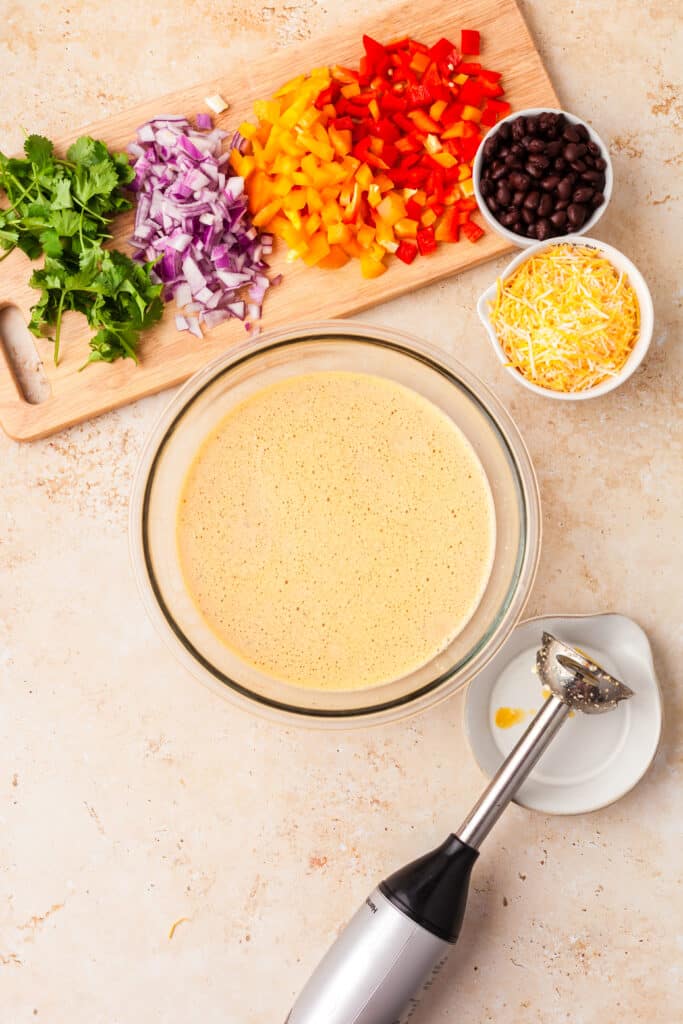 egg mixture in glass bowl with immersion blender next to it.