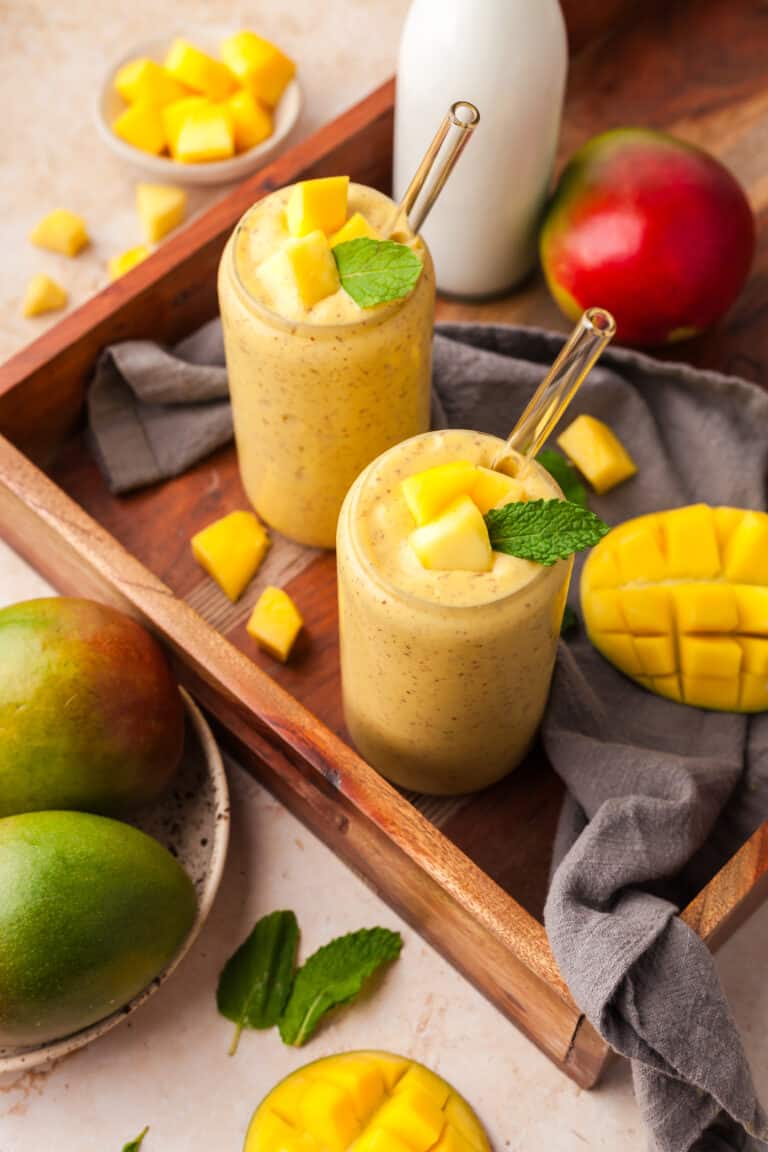 mango protein smoothies in glasses on a wood tray with ingredients surrounding it.