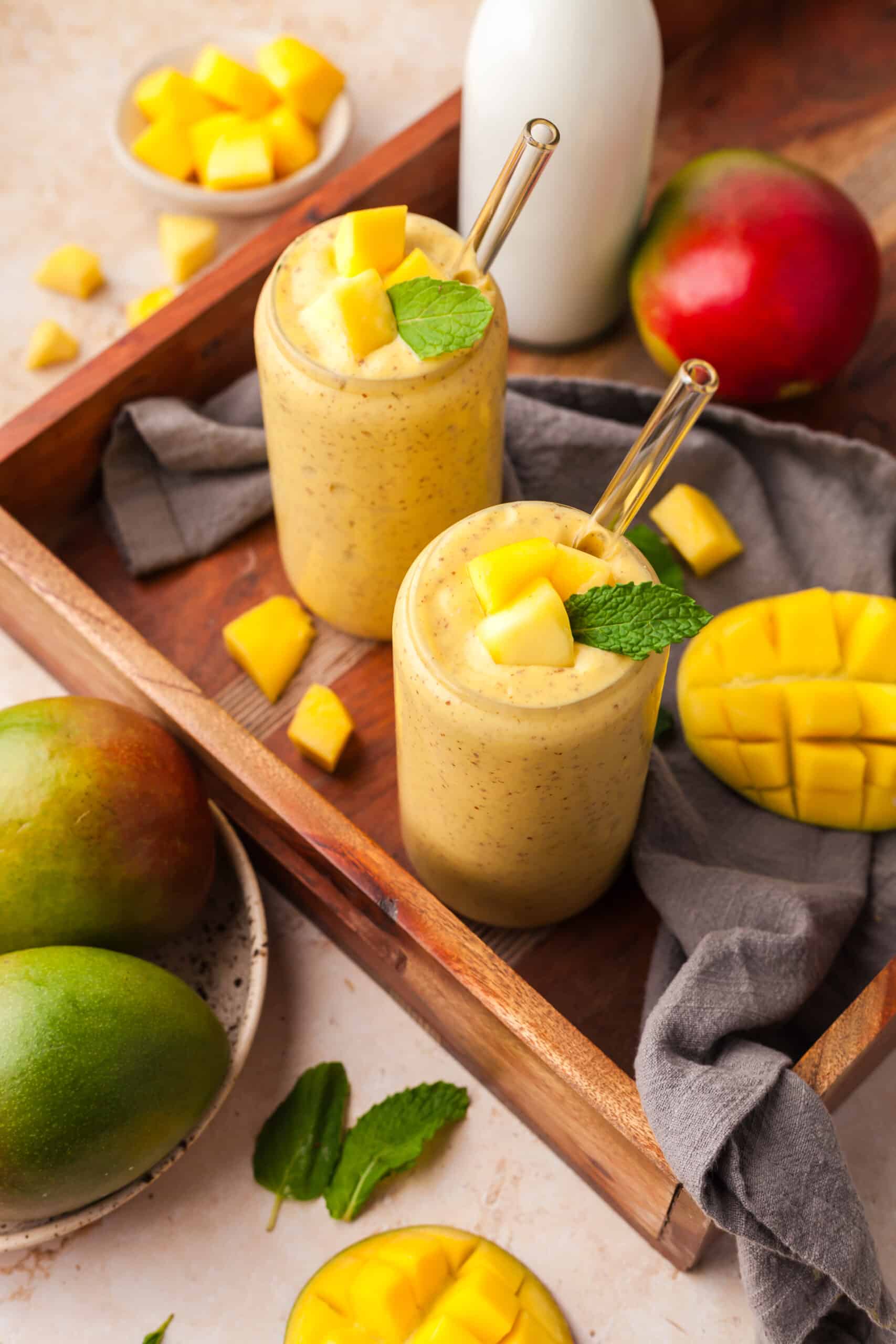 mango protein smoothies in glasses on a wood tray with ingredients surrounding it.