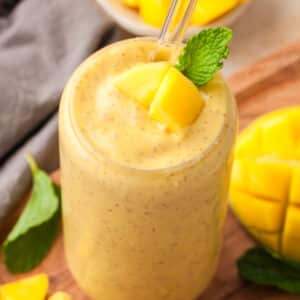mango protein smoothie in a glass with mango chunk and mint leaf garnish.