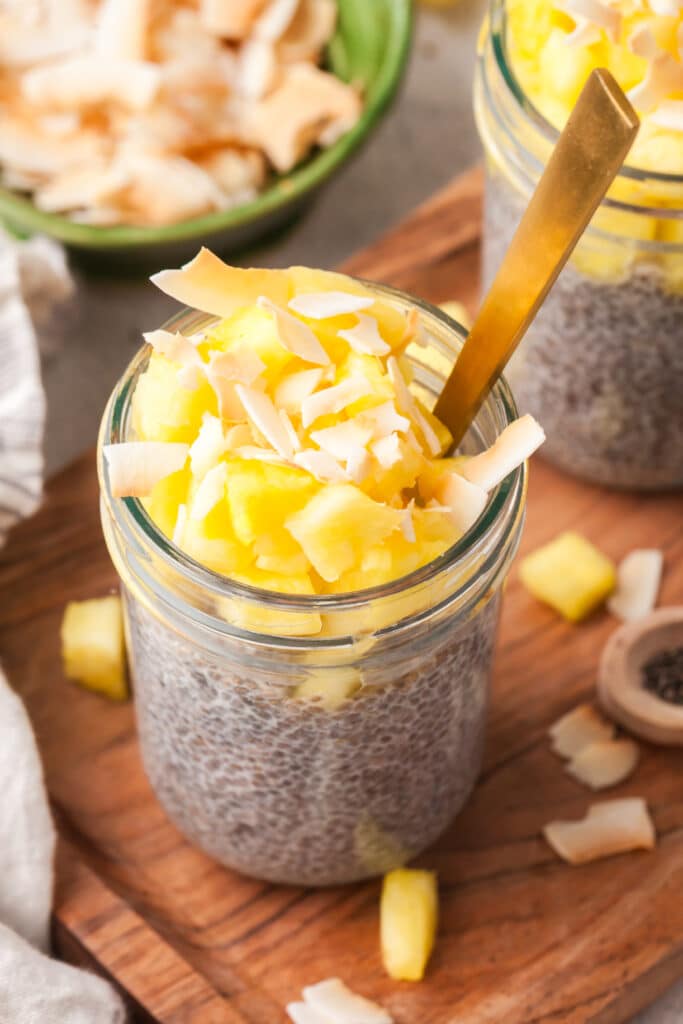 chia seed pudding in jar with pineapple on top and gold spoon inserted.