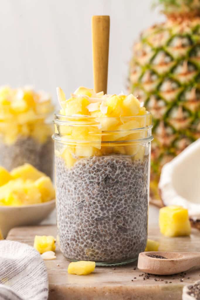 pcos chia pudding in a jar topped with pineapple and coconut shreds with gold spoon.