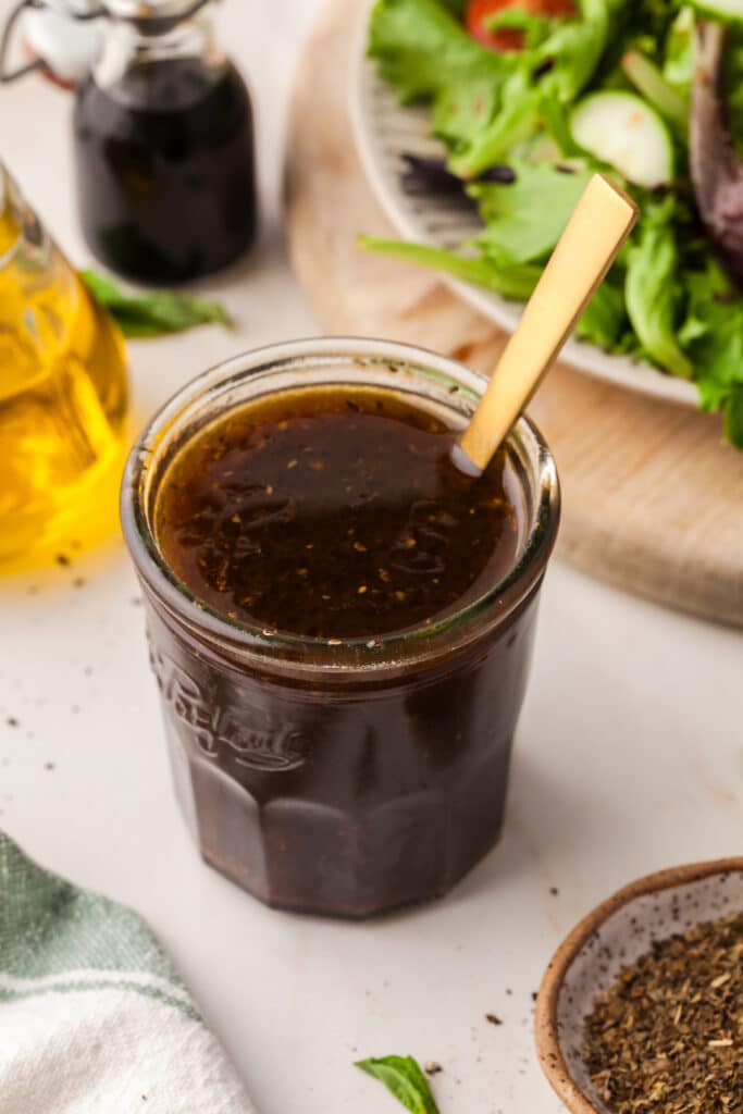 pcos friendly maple balsamic dressing In a mason jar with a spoon inserted.