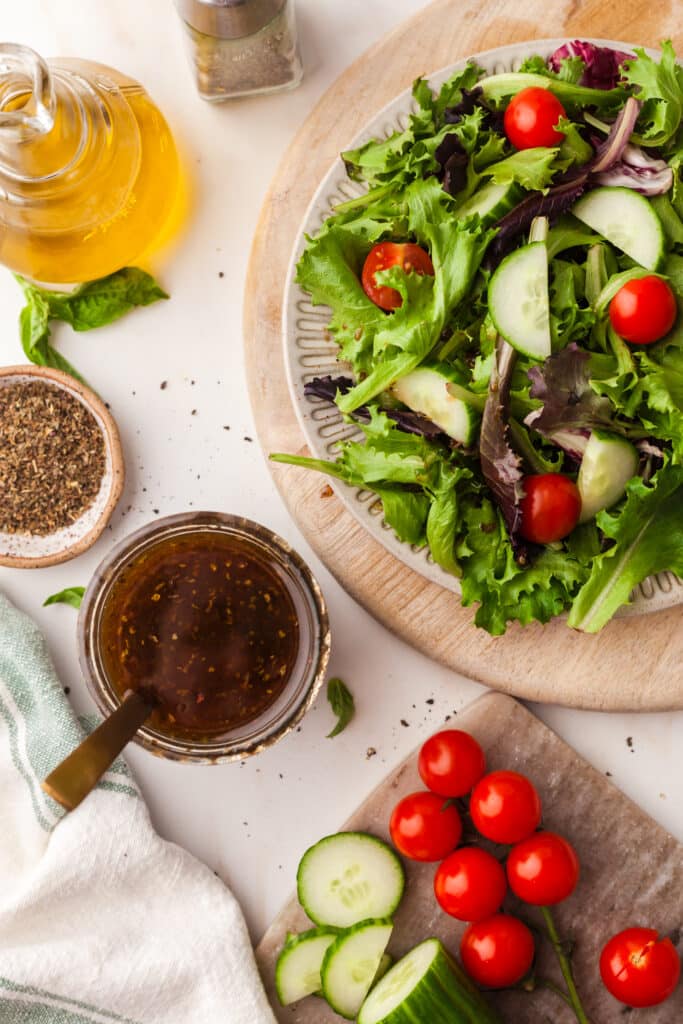 maple balsamic salad dressing in a mason jar with spoon next to a salad and other veggies.