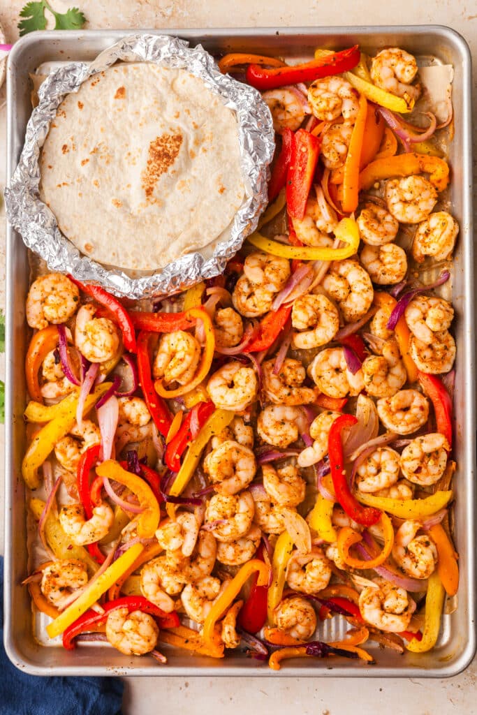 sheet pan shrimp fajitas on baking sheet with tortillas in the corner.