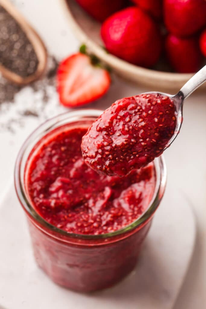 chia seed jam in a mason jar with a spoonful on a spoon being scooped out.