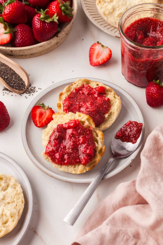chia seed jam on an english muffin with decorative strawberries around.