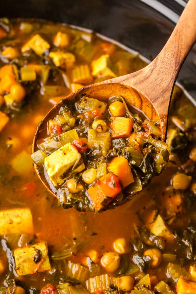golden chickpea and veggie soup close up on a ladle.