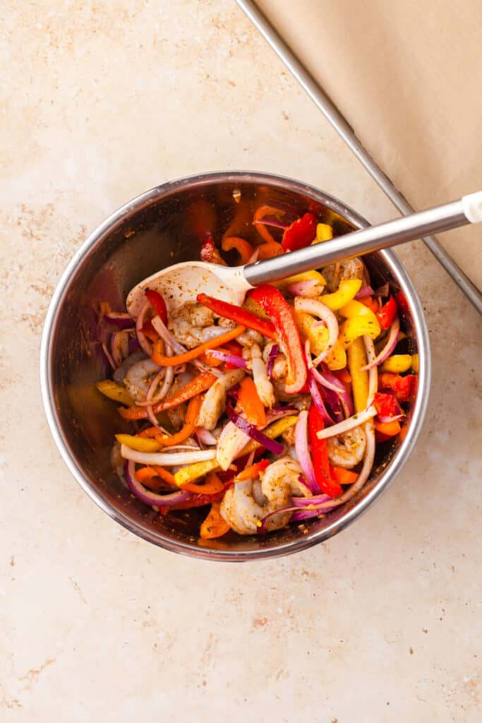 shrimp fajita ingredients mixed around in a large stainless steel bowl.