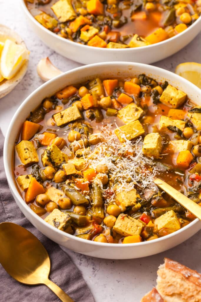 golden chickpea and veggie soup in a bowl with spoon inserted.