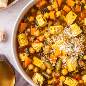 golden chickpea and veggie soup in a bowl with sprinkled parmesan cheese.