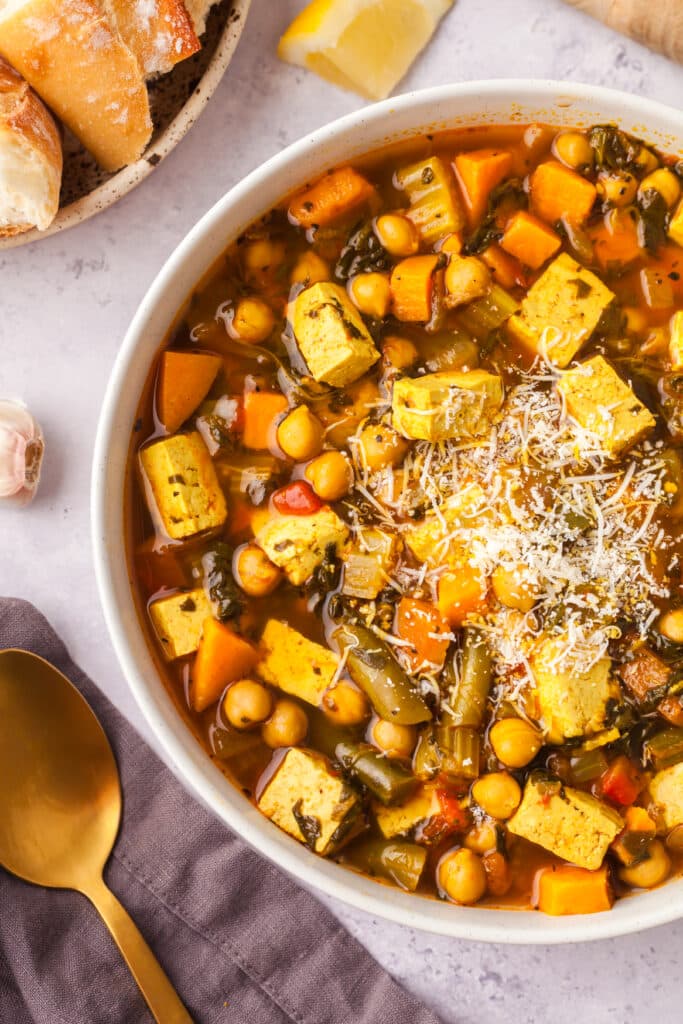 golden chickpea and veggie soup in a bowl with sprinkled parmesan cheese.