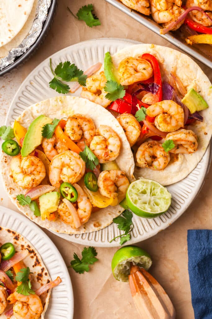 shrimp fajitas in tacos with cilantro, avocado, and jalapenos with squeezed lime nearby.