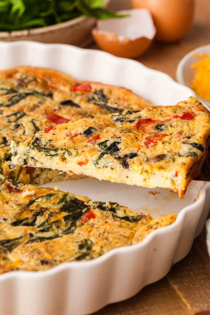 protein crustless quiche in a white pie dish with one slice being removed.