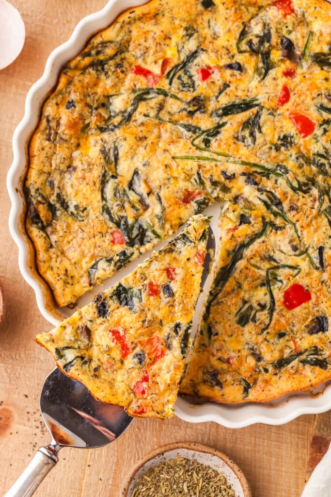 protein crustless quiche in a white pie dish with one slice being removed.