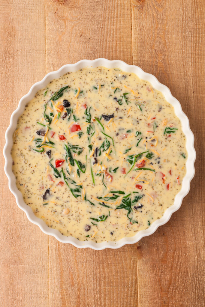 raw crustless quiche in a white pie dish before going into the oven.
