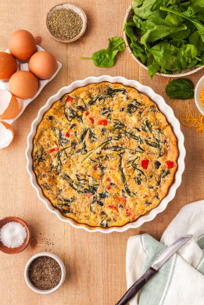 protein crustless quiche in a white pie dish with ingredients around it.