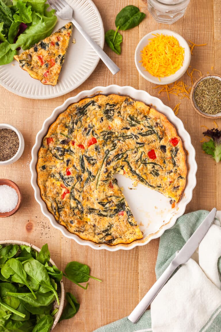 protein crustless quiche in a white pie dish with one slice removed and ingredients around it.