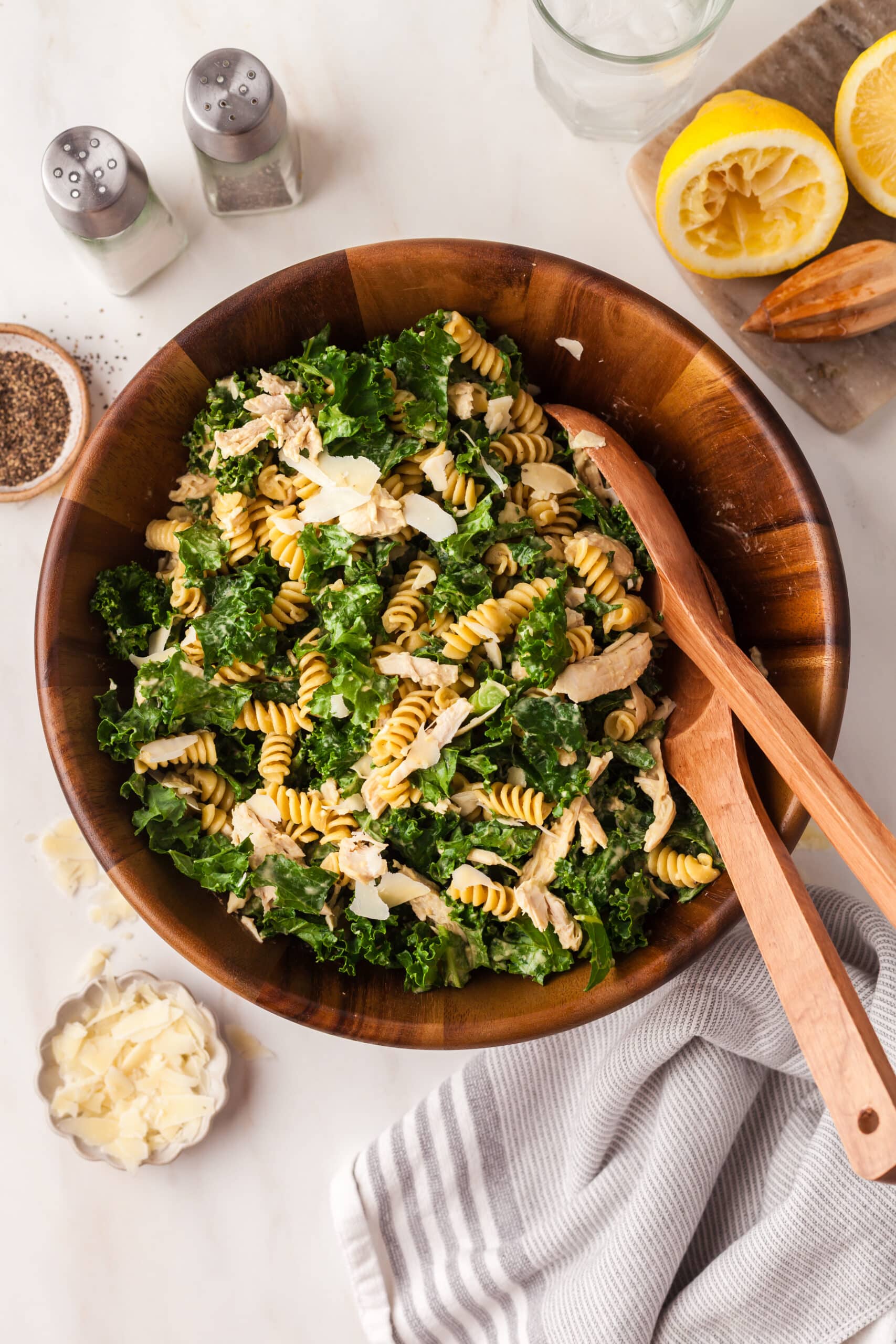 kale pasta caesar salad in a wooden bowl with wooden serving utensils.