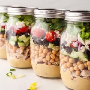mason jar salads lined up on a white countertop.