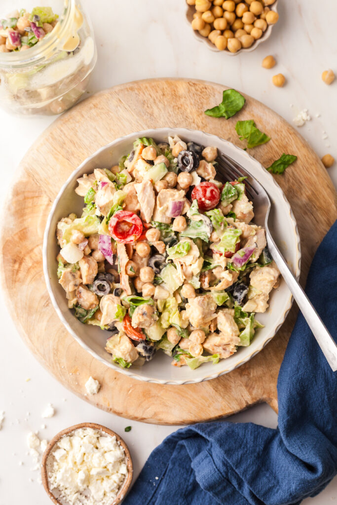 salad in a bowl with fork inserted; sitting on top of a wooden cutting board.