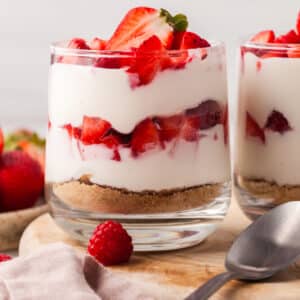 layered protein cheesecake cup with strawberries in a glass jar topped with strawberries and raspberries.