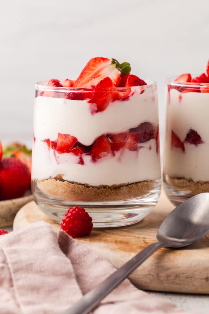 layered protein cheesecake cup with strawberries in a glass jar topped with strawberries and raspberries.
