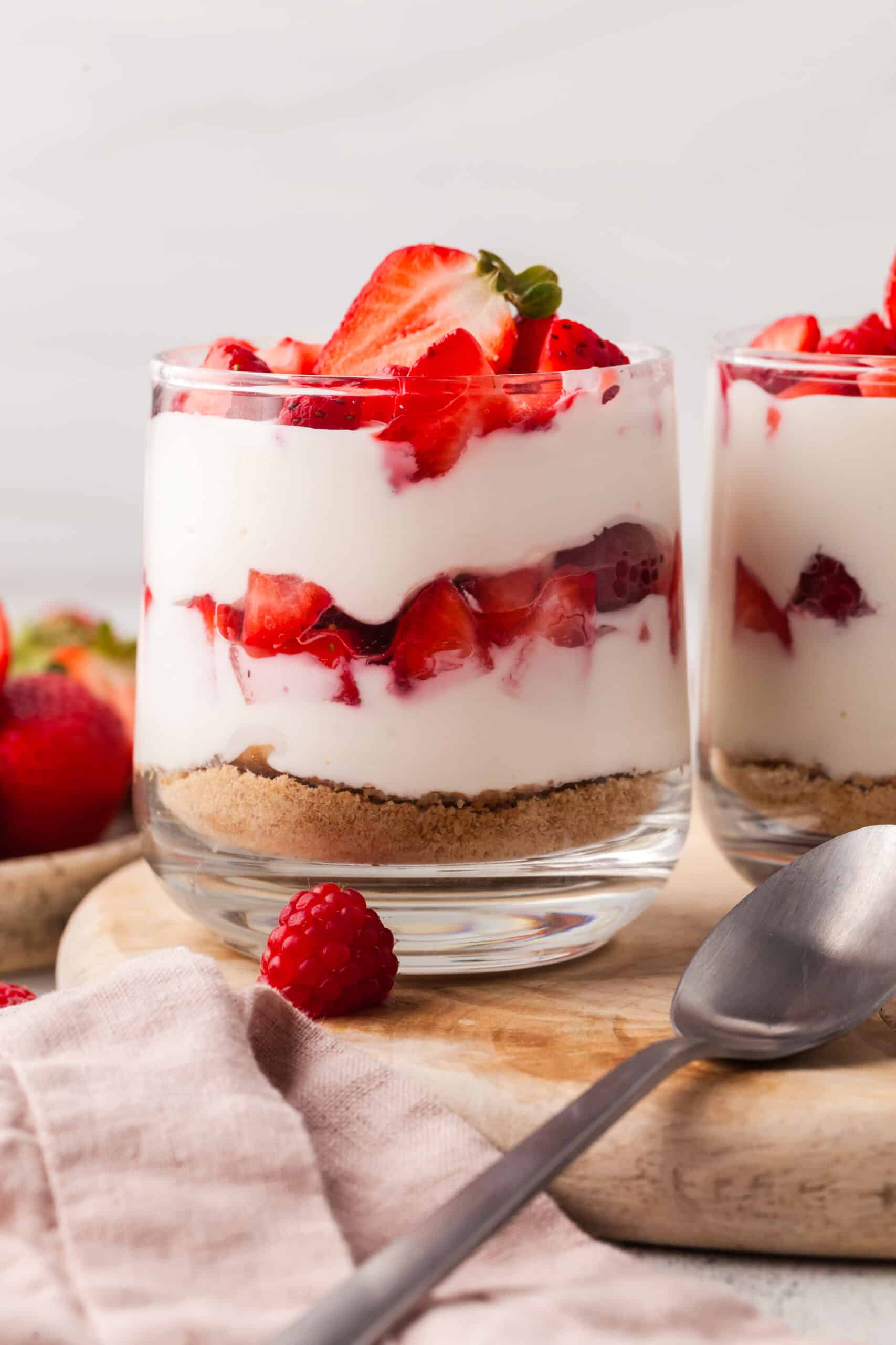layered protein cheesecake cup with strawberries in a glass jar topped with strawberries and raspberries.