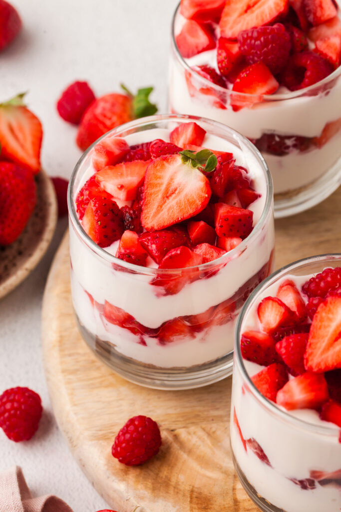 layered protein cheesecake cup with strawberries in a glass jar topped with strawberries and raspberries.